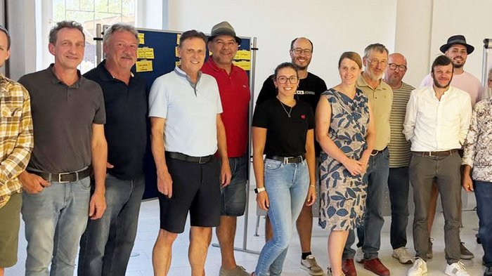 Thema: Generationenwechsel Gruppe von Erwachsenen steht in einem hellen Raum vor einer Pinnwand