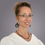 Das lvh-Team Porträt einer lächelnden Frau mit Brille und schwarzen Ohrringen vor grauem Hintergrund