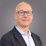 Das lvh-Team Porträt eines lächelnden älteren Mannes mit Brille und Anzug vor grauem Hintergrund