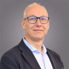 Familiengelder Porträt eines lächelnden älteren Mannes mit Brille und Anzug vor grauem Hintergrund