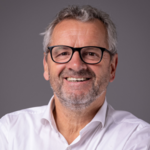 Gröden Lächelnder älterer Mann mit Brille und grauem Haar vor grauem Hintergrund