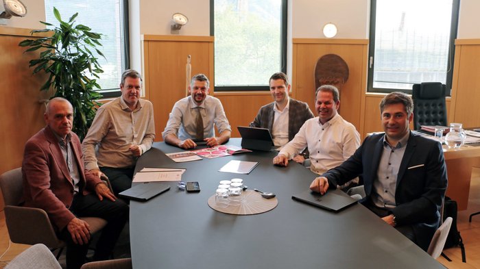 Confronto con il consigliere provinciale Daniel Alfreider: focus sulle soluzioni di mobilità intelligente per il futuro Sei uomini seduti a un tavolo da conferenza in un ufficio con finestre e piante
