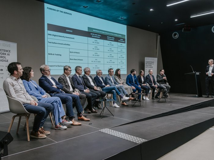 Anlaufstelle für Künstliche Intelligenz vorgestellt Podiumsdiskussion mit mehreren Personen auf der Bühne und Finanzierungsinformationen im Hintergrund