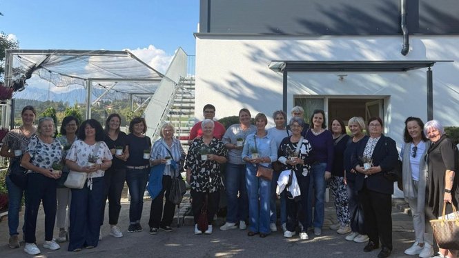 Home Un gruppo di donne e un uomo posa davanti a un edificio e a una serra