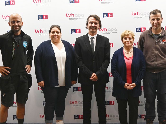 Für die Zukunft: Die Arbeitsgruppe der italienischen Mitglieder im lvh trifft italienischen Bildungsdirektor Fünf Personen posieren vor einer LVH-Generation H Werbewand