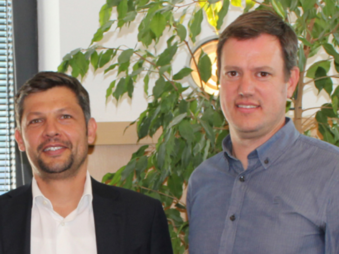 Mehr freie Fahrt für Mietwagen mit Fahrer Zwei Männer in Business-Kleidung vor grüner Pflanze und Fenster