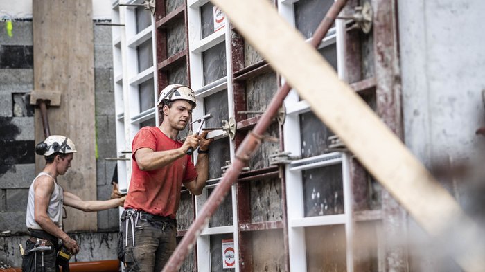 WIFO - Wirtschaftsbarometer Herbst 2024 Baugewerbe Zwei Bauarbeiter mit Helmen arbeiten an einer Baustelle an einer Schalung