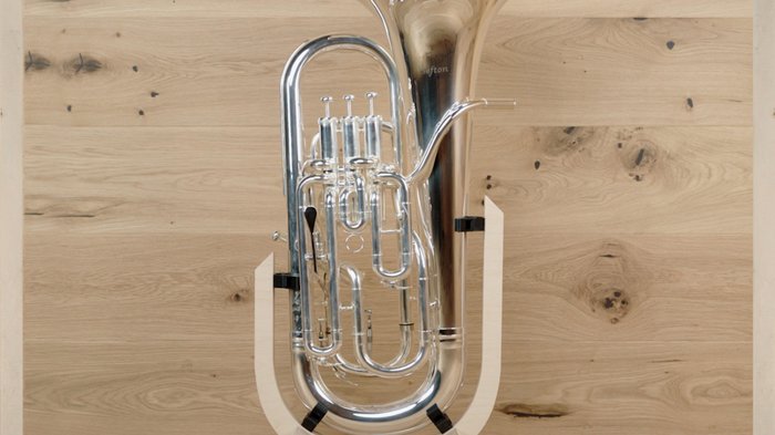 Gleich drei Auszeichnungen in Platin Silbernes Blasinstrument auf einem Holzständer vor Holzwand