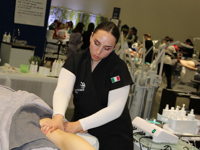 © WorldSkill International Frau mit italienischer Flagge auf Uniform gibt Arm-Massage in Wettkampf