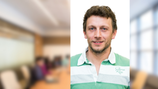 News Porträt eines lächelnden Mannes in Freizeitkleidung mit unscharfem Bürohintergrund