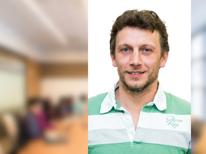 Una nuova e forte generazione di artigiani a Postal Ritratto di uomo sorridente con abbigliamento casual, sfondo ufficio sfocato