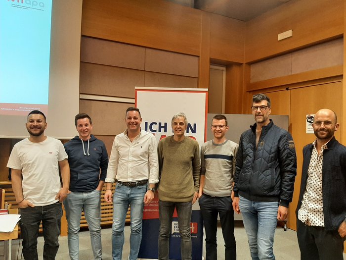 Führungswechsel Sieben Männer stehen nebeneinander in einem Konferenzraum vor einem Banner