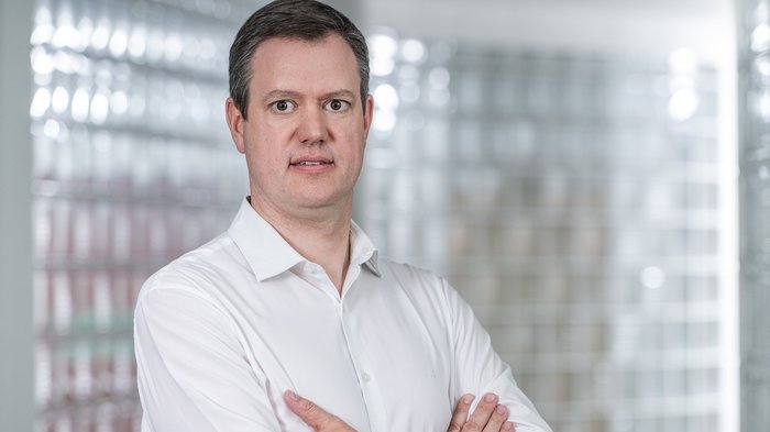 Premio Economia 2024 Uomo con camicia bianca con le braccia incrociate davanti a sfondo chiaro