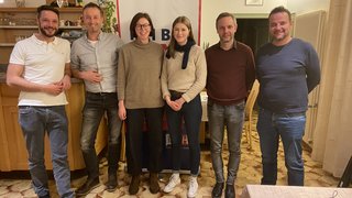 News Sechs lächelnde Personen stehen in einem Raum vor einem Banner