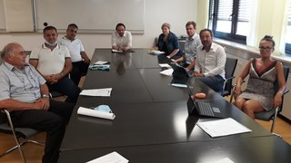 News Neun Personen in einem Besprechungsraum an einem langen schwarzen Tisch