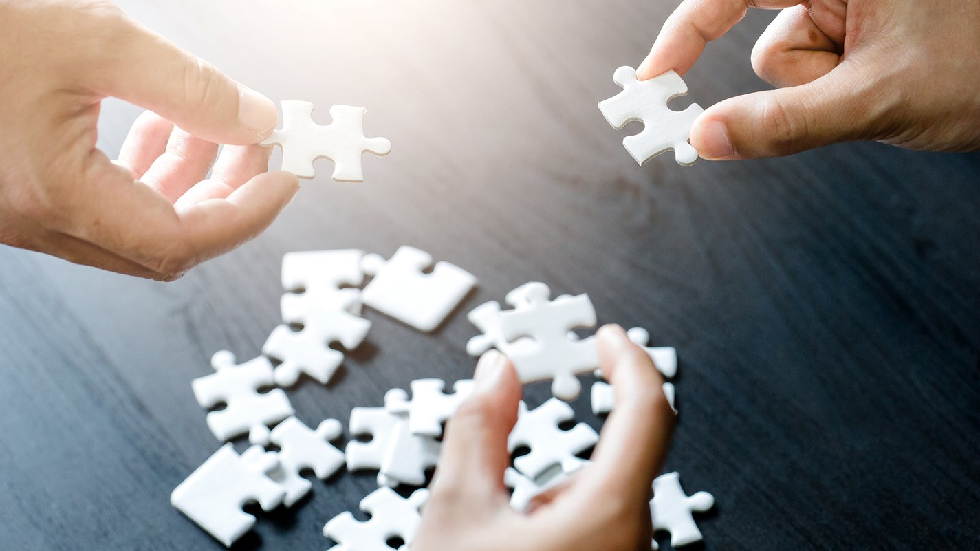 Home Mani che tengono pezzi di puzzle bianchi sopra un tavolo