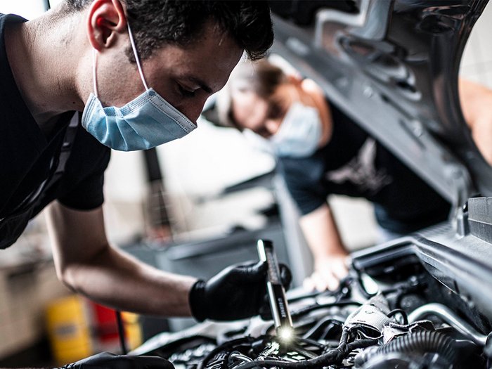 Auf dem neusten Stand der Technik Mechaniker überprüfen Motor im geöffneten Auto mit Taschenlampe und Maske
