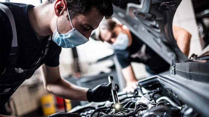 Auf dem neusten Stand der Technik Mechaniker überprüfen Motor im geöffneten Auto mit Taschenlampe und Maske