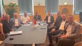 News Neun Männer in einem Besprechungsraum an einem großen Tisch mit italienischer Flagge