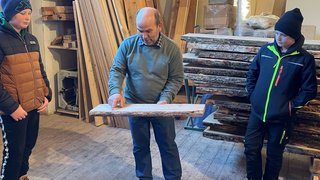 News Mann zeigt Kindern ein Holzbrett in einer Holzwerkstatt