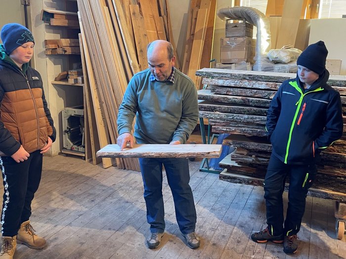 Mittelschule Toblach: Traumberufe in Gastgewerbe und Handwerk vorgestellt Mann zeigt Kindern ein Holzbrett in einer Holzwerkstatt