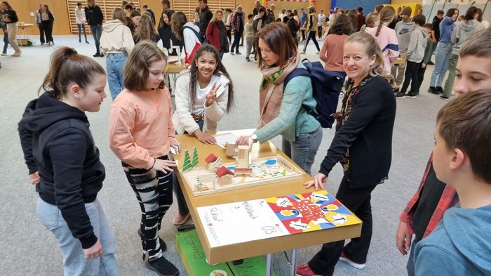 Schulprojekt "Clever gebaut": Selbst entwickelte Spiele prämiert Kinder und Lehrerinnen zeigen ein Holzmodell bei einem Schulprojekt in der Turnhalle
