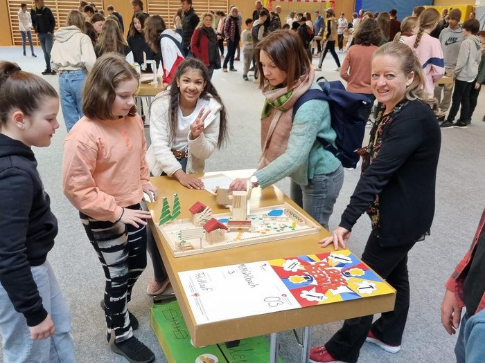 Schulprojekt "Clever gebaut": Selbst entwickelte Spiele prämiert Kinder und Lehrerinnen zeigen ein Holzmodell bei einem Schulprojekt in der Turnhalle