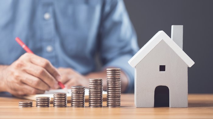 Haushaltsgesetz 2026: Was sich für Betriebe und Beschäftigte ändert Münzstapel wachsen neben einem Modellhaus auf einem Schreibtisch