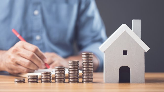 Home Monete impilate in crescita accanto a una casetta in miniatura su una scrivania