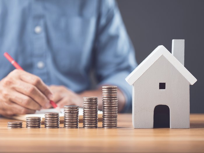 Haushaltsgesetz 2026: Was sich für Betriebe und Beschäftigte ändert Münzstapel wachsen neben einem Modellhaus auf einem Schreibtisch