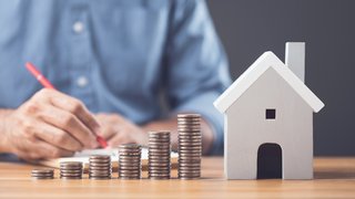 News Monete impilate in crescita accanto a una casetta in miniatura su una scrivania