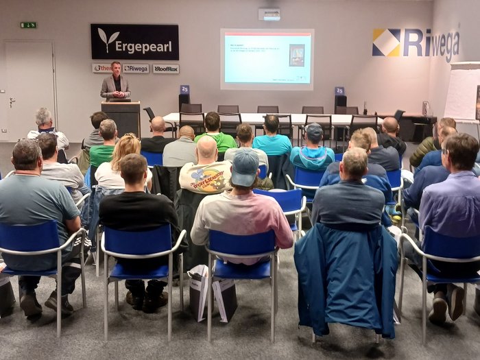 Jährlicher Pflichtkurs der Kaminkehrer/innen Person hält Vortrag vor Publikum in Konferenzraum mit Firmenlogos an der Wand
