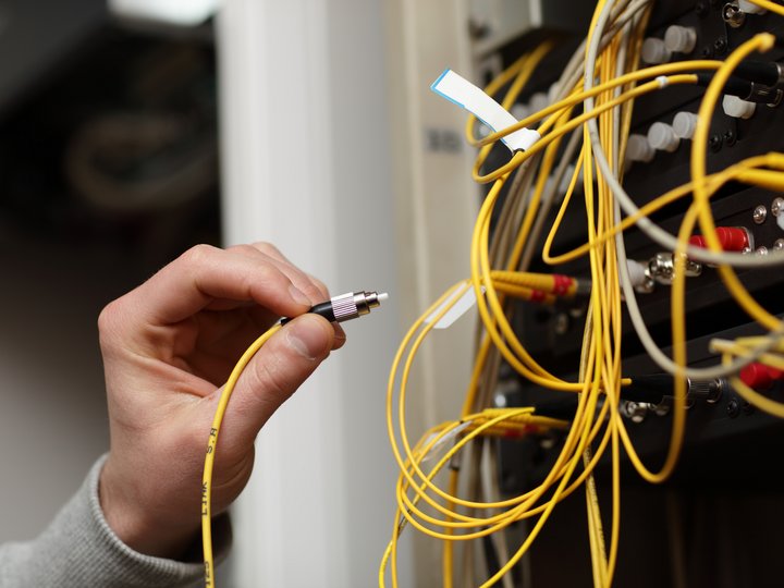 Percorso formativo Mano che tiene un cavo in fibra ottica giallo vicino a una porta di rete