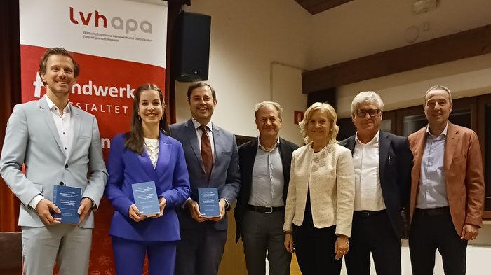 Einblick in den neuen Vergabekodex: Erfolgreicher Infoabend Sieben Personen in Anzügen posieren vor einem LVH-Banner mit Büchern in der Hand