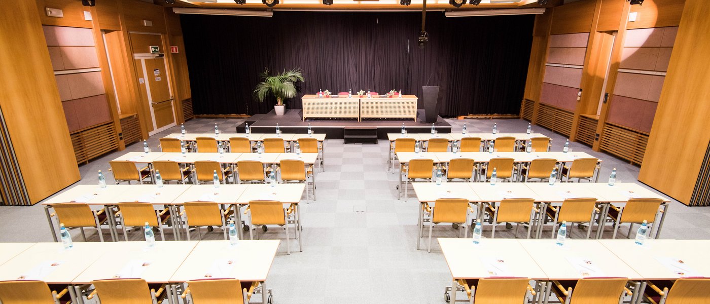 Affitto aule seminari Sala conferenze con file di sedie e palco con tende nere