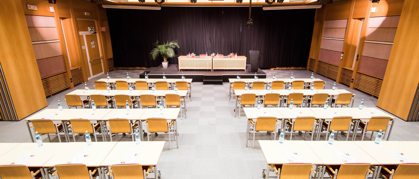Vermietung Seminarräume Konferenzraum mit Stuhlreihen und Bühne mit schwarzen Vorhängen