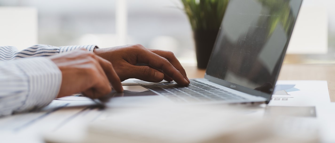 Webinar - Mitarbeiterbindung Hände tippen auf einer Laptop-Tastatur an einem hellen Arbeitsplatz