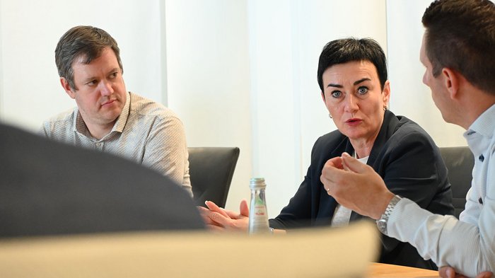 Wohnen muss leistbar sein! Herausforderungen und Lösungsansätze in Südtirol Drei Personen führen eine lebhafte Diskussion in einem Büro
