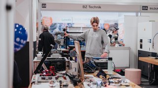 News Junger Mann bedient einen Roboterarm auf einer Technikmesse