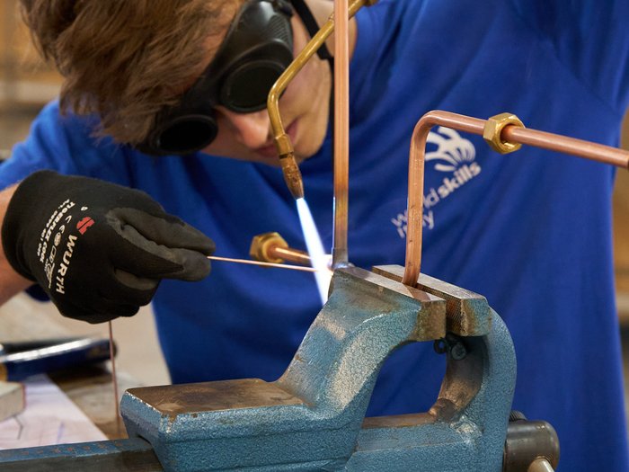 WorldSkills Italy: Lyon als Ziel Person schweißt Kupferrohre mit Brenner und Schutzbrille