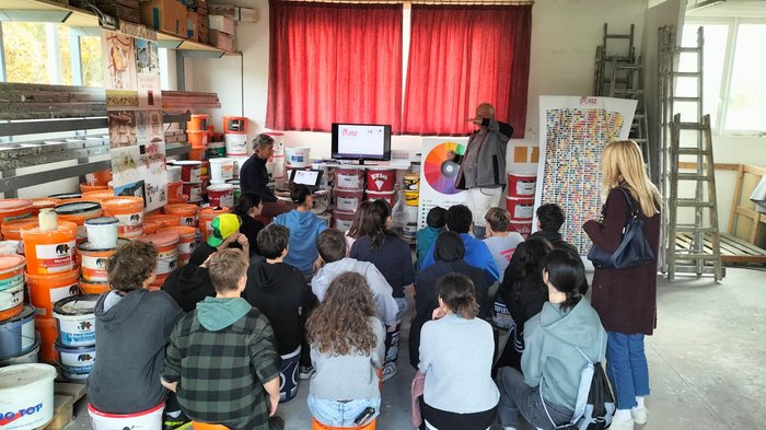 Im Auftrag der Berufe quer durchs Unterland Kinder sitzen auf Eimern bei einer Farbwerkstatt und hören einem Vortrag zu