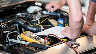 News Person überprüft Autoschaltplan mit Multimeter unter der Motorhaube