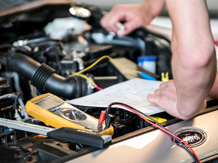 Kfz-Mechatroniker empfehlen „Urlaubs-Check“ Person überprüft Autoschaltplan mit Multimeter unter der Motorhaube