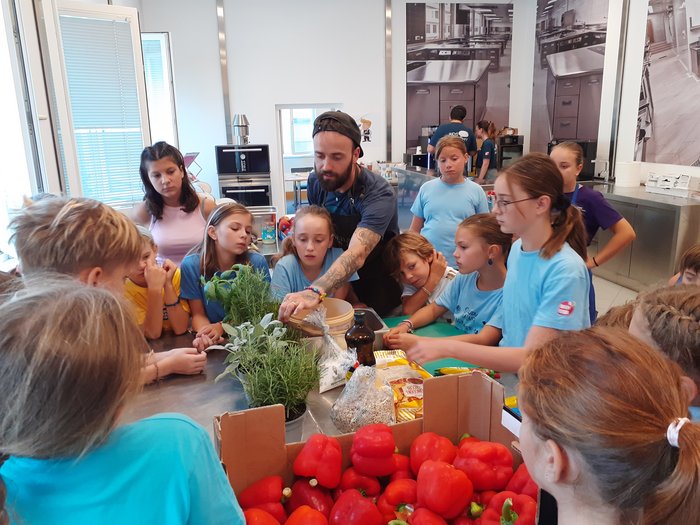 Kids-Academy 2024: Das große Finale Kinder und Mann lernen in einer Küche mit frischen Paprikaschoten und Kräutern