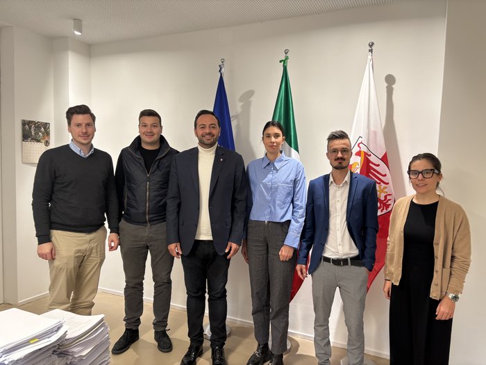 Incontro Galateo con JH e HGJ Sei persone in piedi davanti a tre bandiere in un ufficio