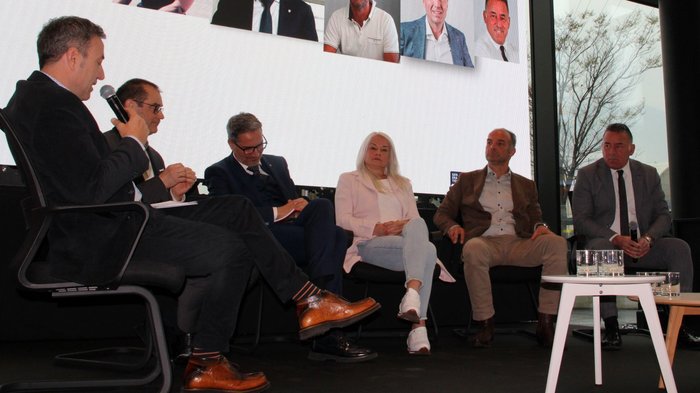 Focus sulle sfide e le prospettive future del trasporto merci transalpino Discussione sul palco con sei persone sedute davanti a uno schermo grande con ritratti