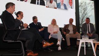 News Podiumsdiskussion mit sechs Teilnehmern vor großem Bildschirm mit Porträts