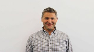 News Mann mittleren Alters mit kariertem Hemd lächelt vor weißer Wand