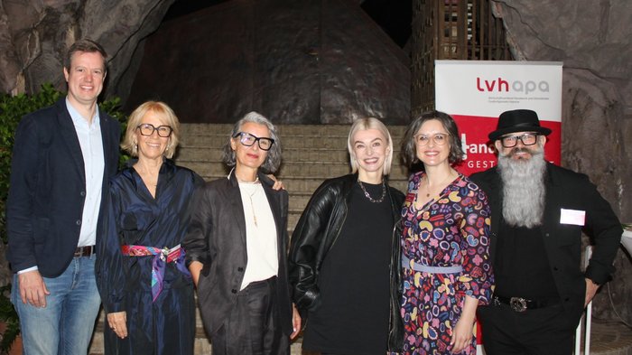Attivi e orientati al futuro: l'artigianato di Ora Foto di gruppo di sei persone davanti a un arco di roccia e un banner LVH-Apa