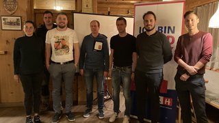 News Sieben Personen in einem Raum mit Holzwänden vor Projektor und Werbebanner